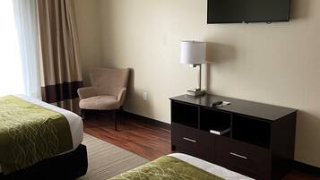 Habitación de hotel con dos camas, una silla, un escritorio con lámpara y un televisor en la pared.