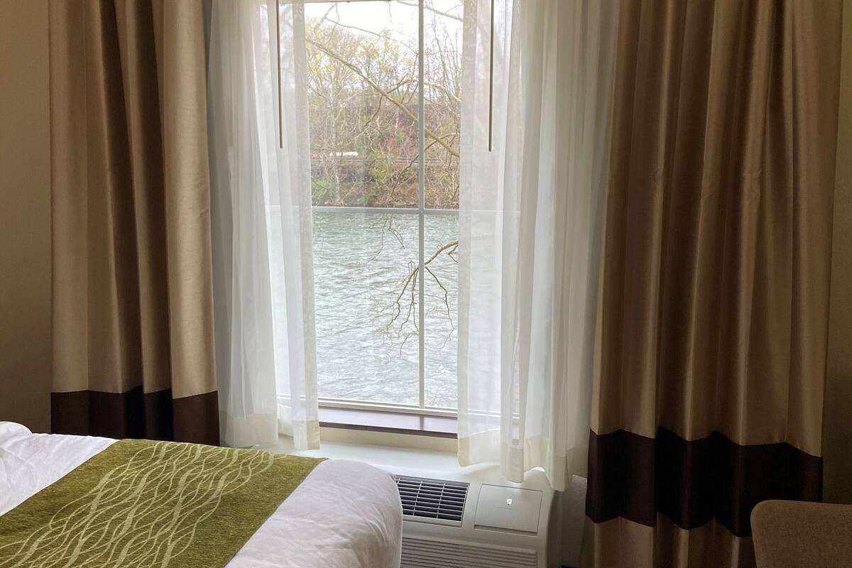 A hotel room with a bed, a window with curtains, and a view of a body of water.
