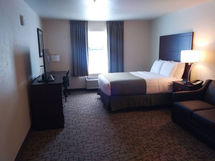 A hotel room with a bed, a desk, a chair, a lamp, and a window with curtains.