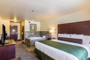 A hotel room with a large bed, a wooden headboard, a built-in bathtub, a desk with a flat-screen TV, and a framed picture on the wall. - Cobblestone Inn & Suites - Barron (Barron)