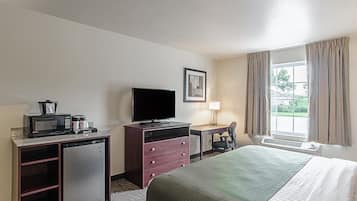 Una habitación de hotel con una cama, un escritorio con silla, televisor, microondas y refrigerador.