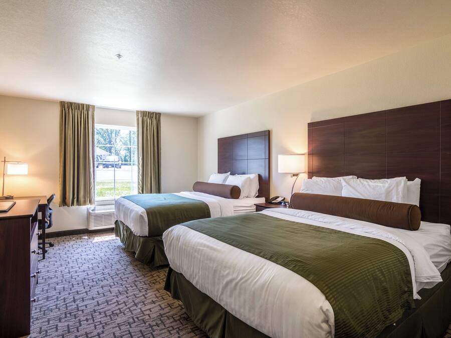 A hotel room with two beds, a desk, a chair, a TV, and a window with curtains.