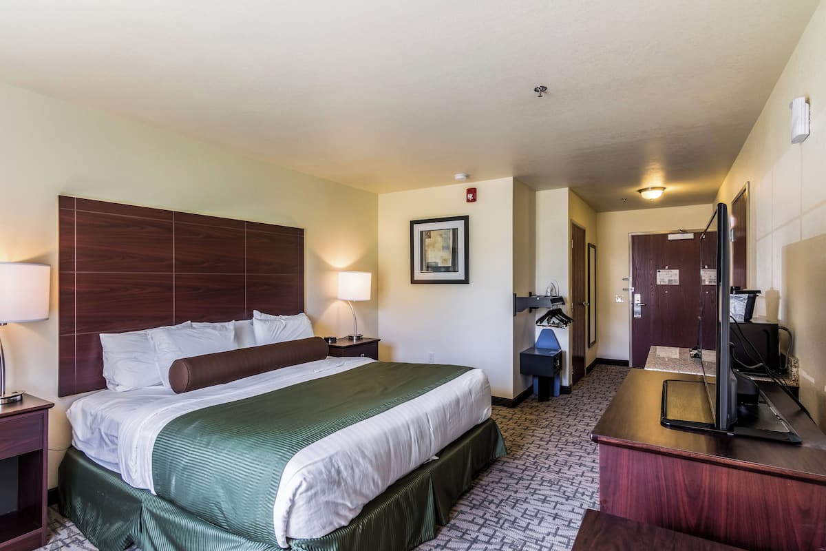 Ein Hotelzimmer mit einem großen Bett, einem Schreibtisch mit Computer, einem Spiegel und einer Tür zum Badezimmer.