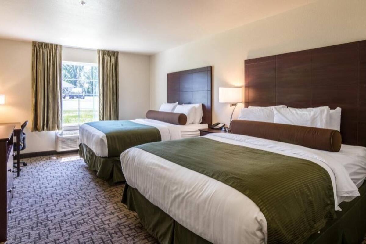 Ein Hotelzimmer mit zwei Betten, einem Schreibtisch, einem Sessel, einem Fernseher und einem Fenster mit Vorhängen.