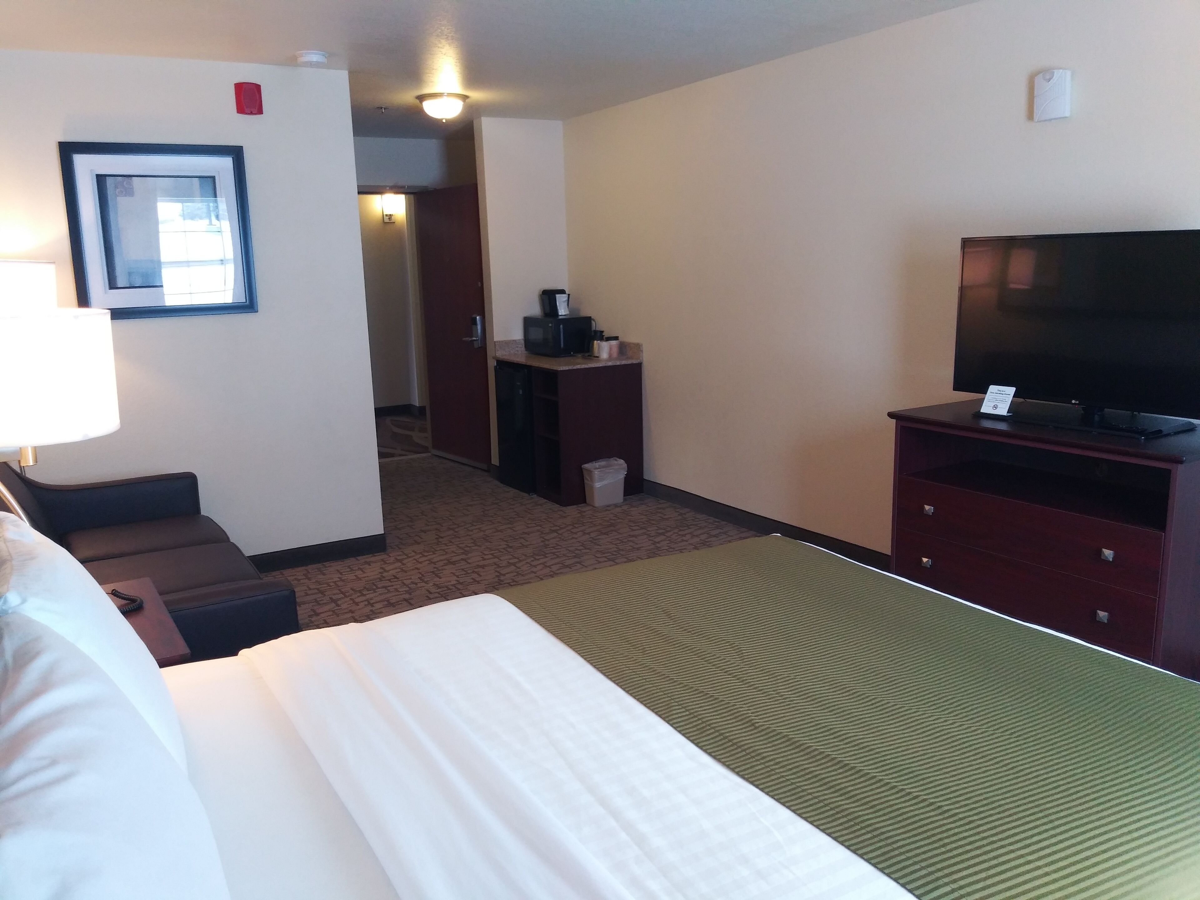 Habitación de hotel con una cama, un televisor sobre un mueble bajo, un escritorio con microondas y una silla.