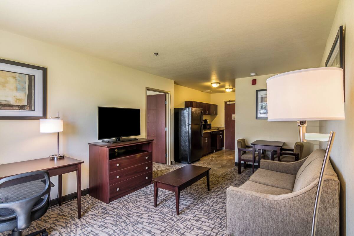 Ein Hotelzimmer mit Schreibtisch, Stuhl, Sofa, Fernseher, Kühlschrank und Küchenzeile.
