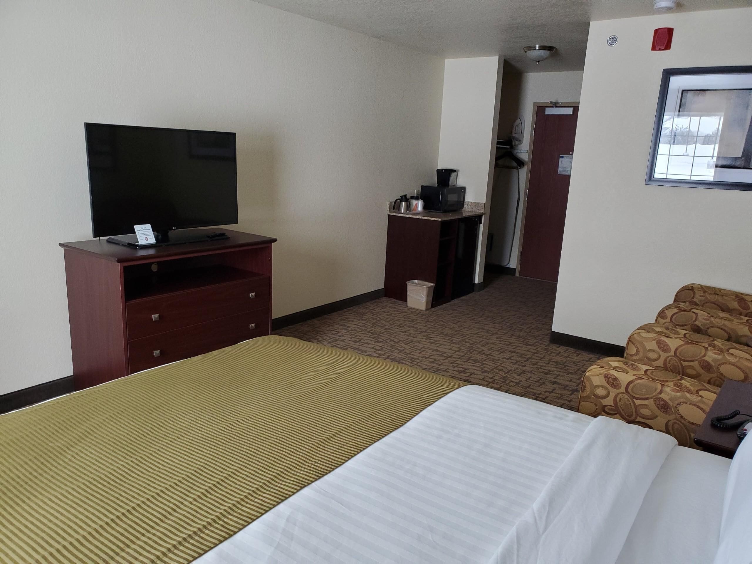 Habitació d'hotel amb llit, televisió sobre un suport de fusta, petita cuineta i sofà estampat.