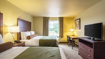 A hotel room with two beds, a desk, a television, and a window with curtains.