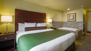 Habitación de hotel con una cama grande, dos lámparas de noche, una mesita de noche, una colcha verde, una pared de mármol, un cuadro enmarcado, un baño con bañera y un piso de baldosas.