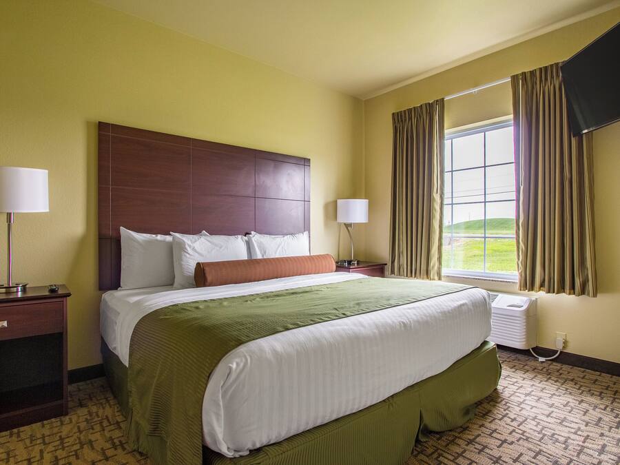 Una habitación de hotel con una cama grande, dos mesitas de noche, un televisor y una ventana con cortinas.