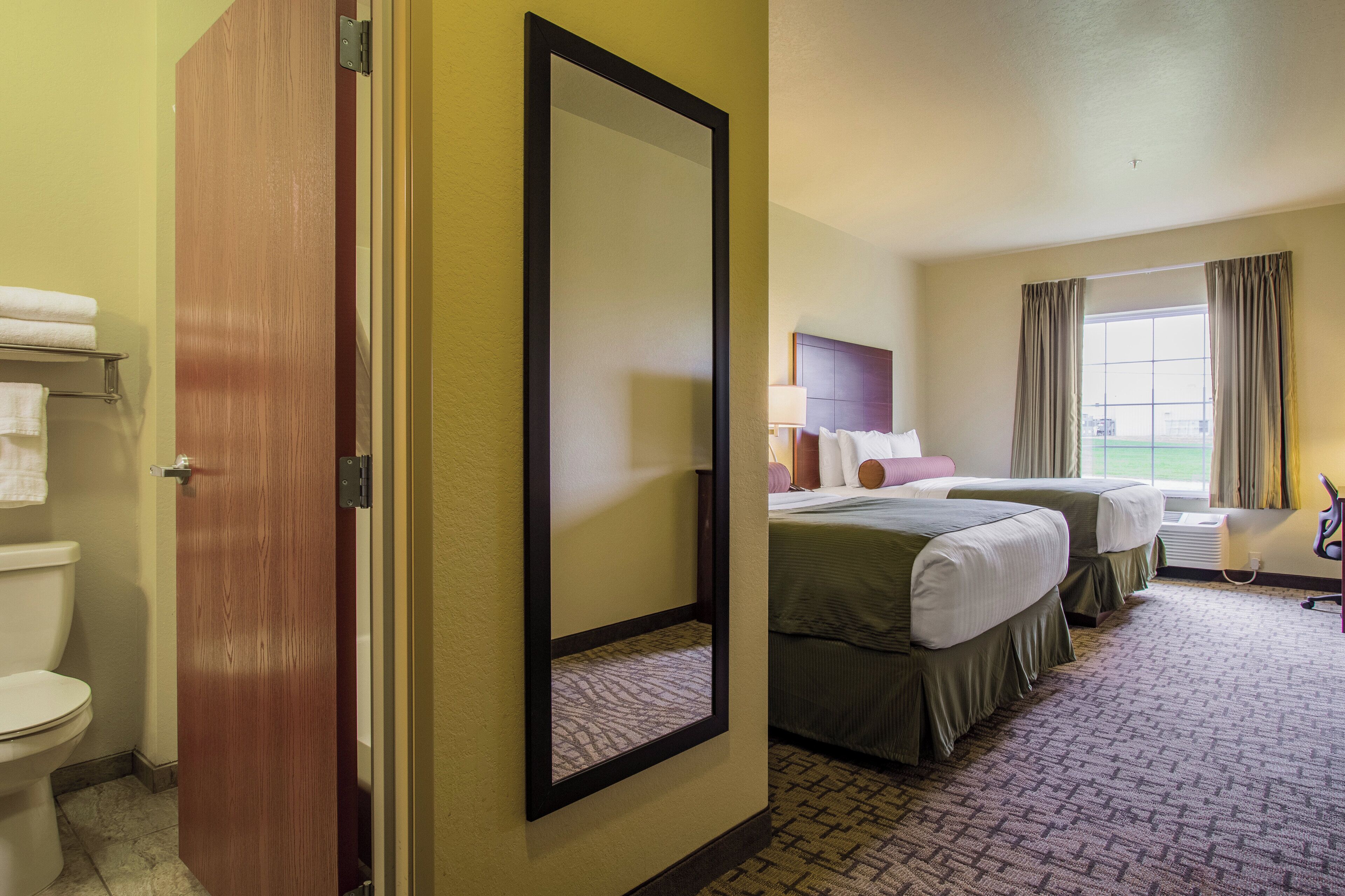 Une chambre d’hôtel avec deux lits, une salle de bain et une fenêtre avec des rideaux.