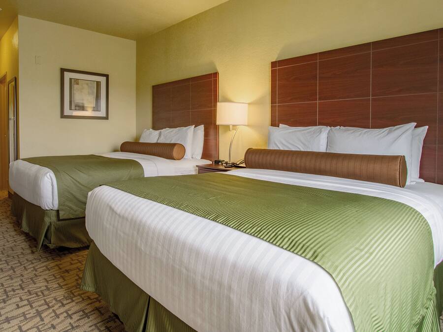 Una habitación de hotel con dos camas, una mesita de noche con lámpara y un cuadro enmarcado en la pared.