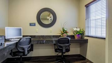 A hotel reception area with two black office chairs, a desktop computer, a large mirror, and a sign indicating the business center.