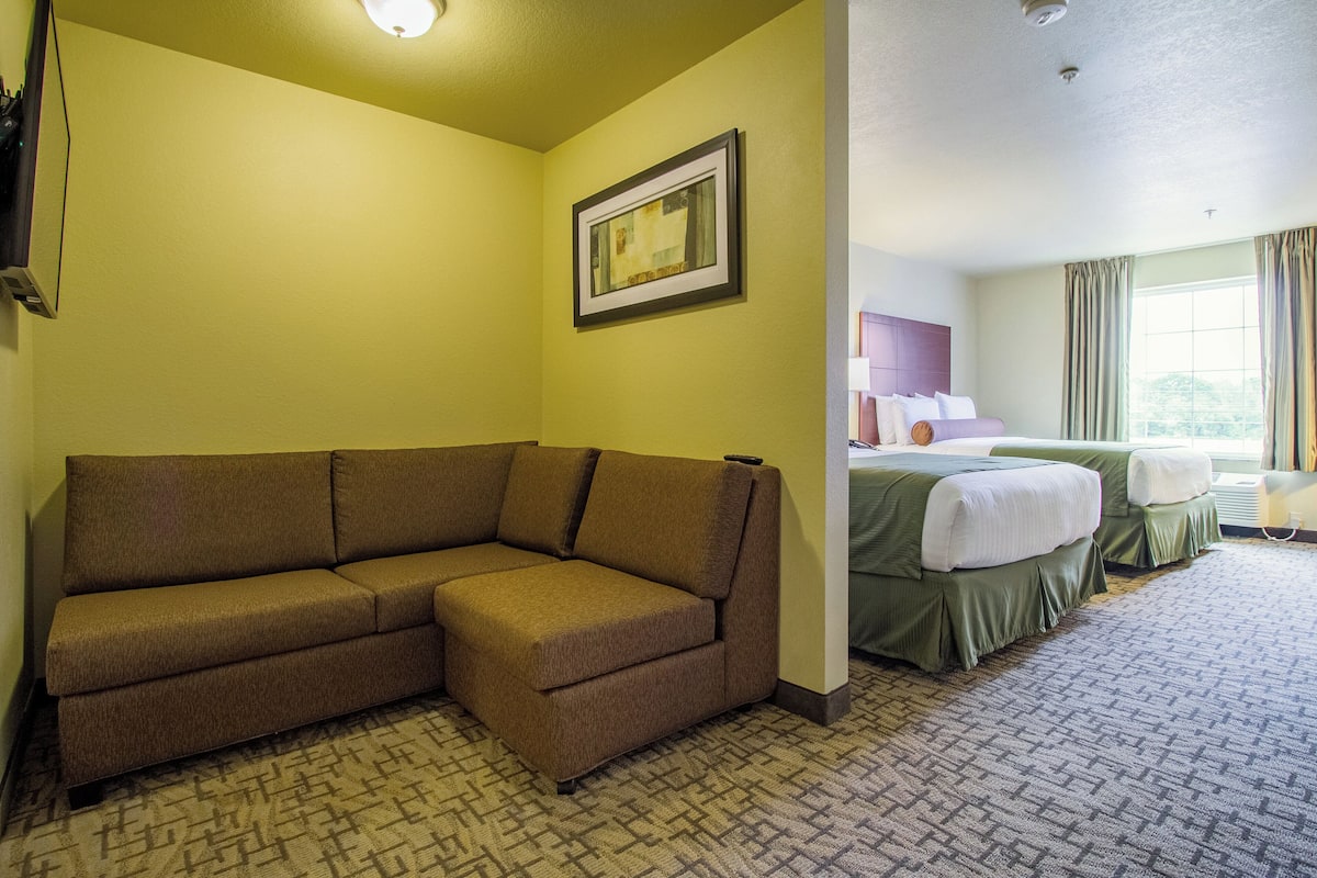 Une chambre d’hôtel avec un canapé d’angle, un lit avec une literie verte et un tableau encadré au mur.