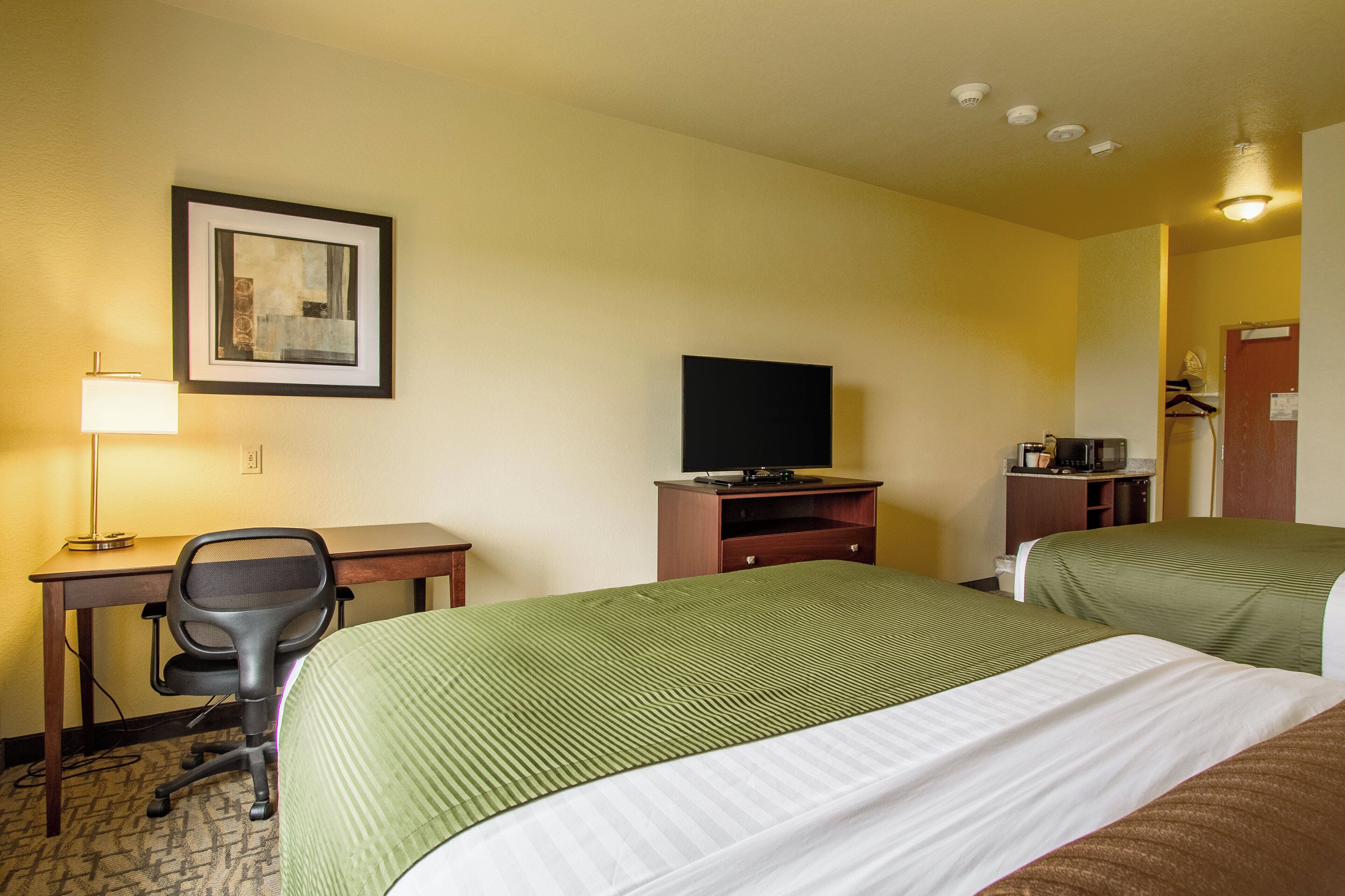 Habitación de hotel con dos camas, un escritorio con silla, televisión y un cuadro en la pared.