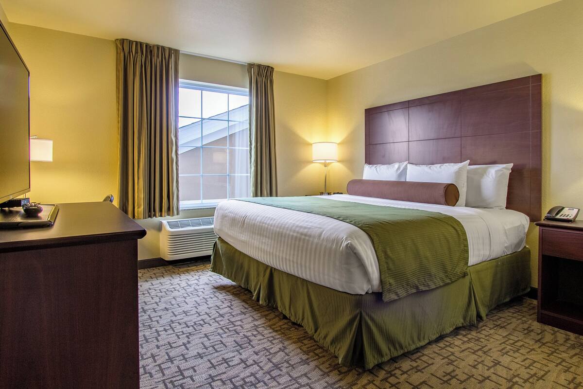 Une chambre d’hôtel avec un grand lit, un bureau, une lampe et une fenêtre avec des rideaux.