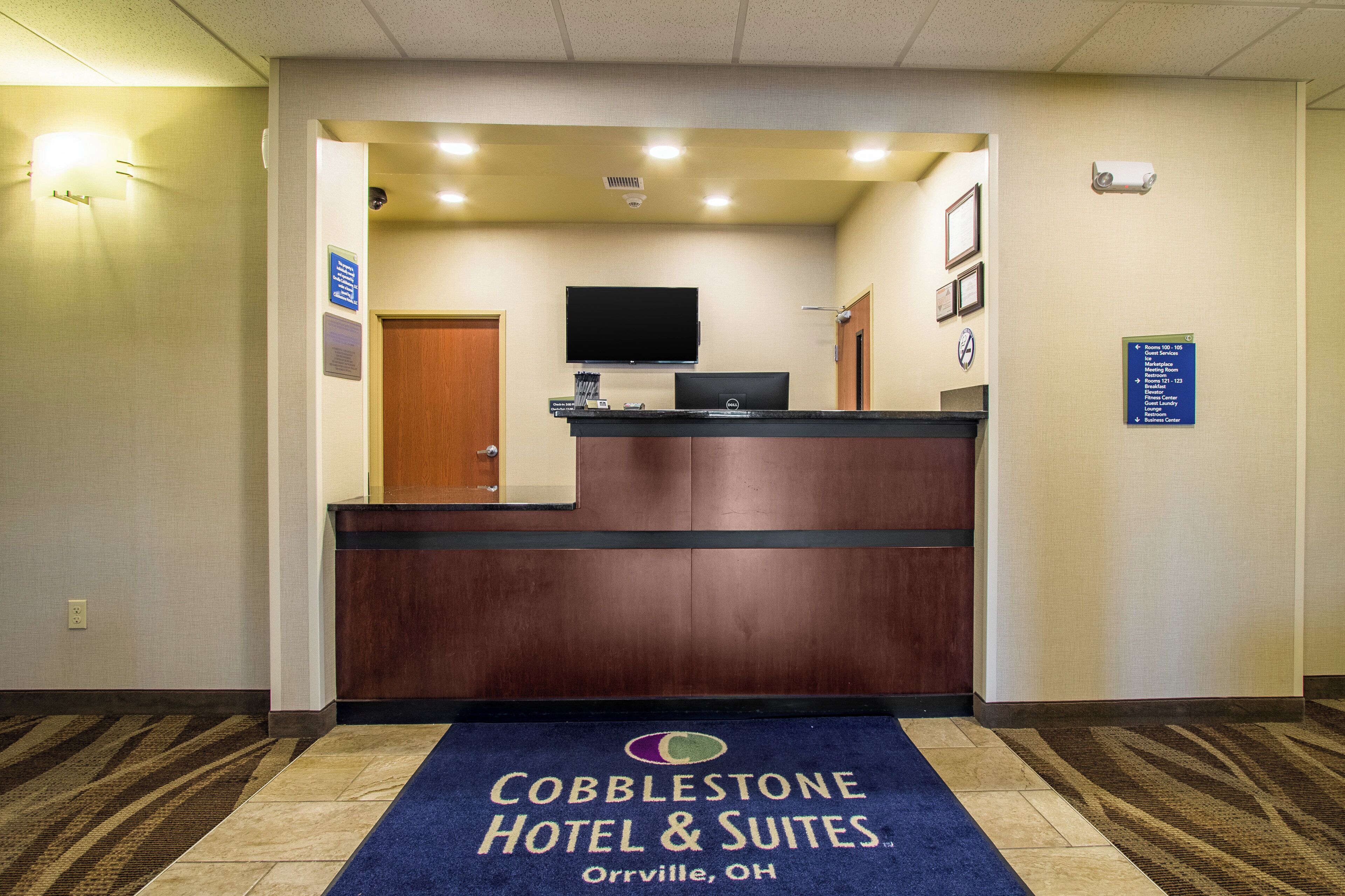 En hotellobby med en receptionsdisk, en platt-TV och en skylt som visar hotellets namn och adress.