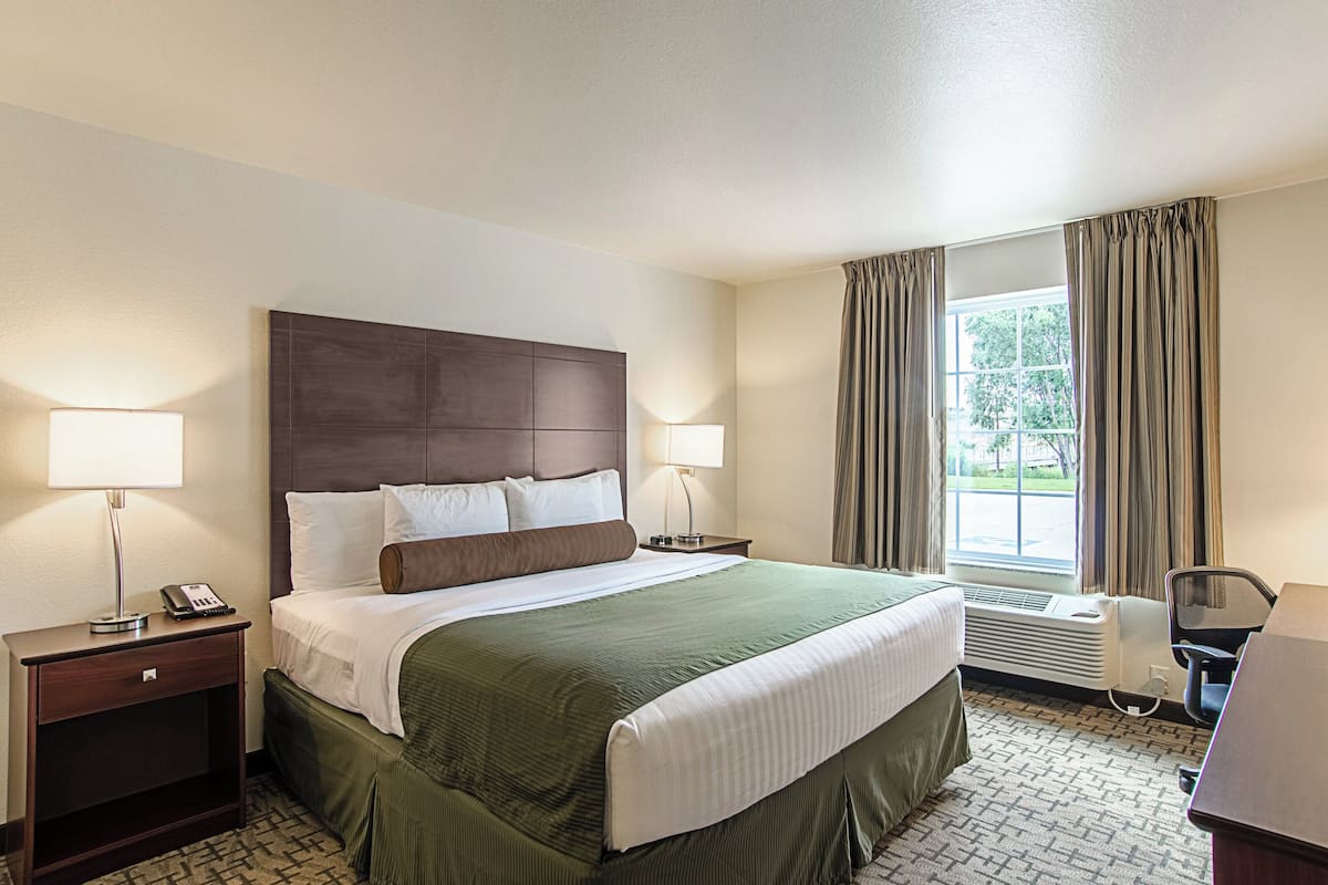 A hotel room with a large bed, two bedside tables with lamps, a chair, and a window with curtains.