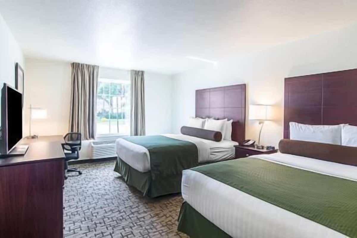 A hotel room with two beds, a desk, a chair, a TV, and a window with curtains.