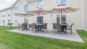 A patio area with outdoor seating and umbrellas, a building with multiple windows, and a grassy lawn. - Cobblestone Inn & Suites - Guernsey (Guernsey)