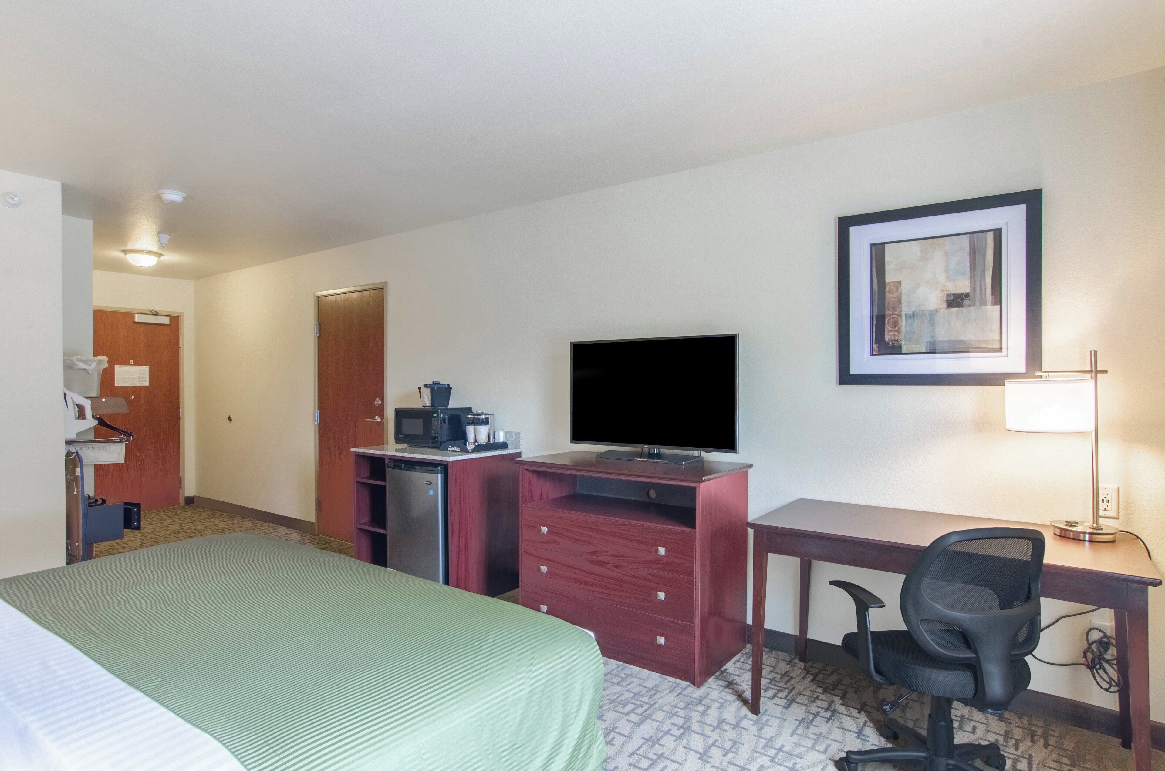 A hotel room with a bed, desk, television, and a small kitchenette.