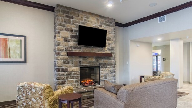 A living room with a stone fireplace, a flat-screen TV, patterned sofas, and a small round table. - Cobblestone Inn & Suites - Guernsey (Guernsey)