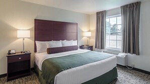 A hotel room with a large bed, two bedside tables with lamps, a window with curtains, and a radiator. - Cobblestone Inn & Suites - Guernsey (Guernsey)