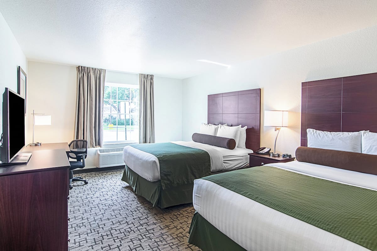 A hotel room with two beds, a desk, a chair, a TV, and a window with curtains.