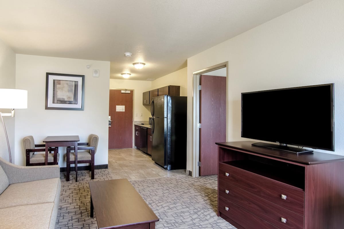 A compact living space with a kitchenette, a flat-screen TV, a sofa, a dining table, and a coffee table.