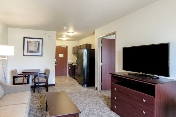 A compact living space with a kitchenette, a flat-screen TV, a sofa, a dining table, and a coffee table.