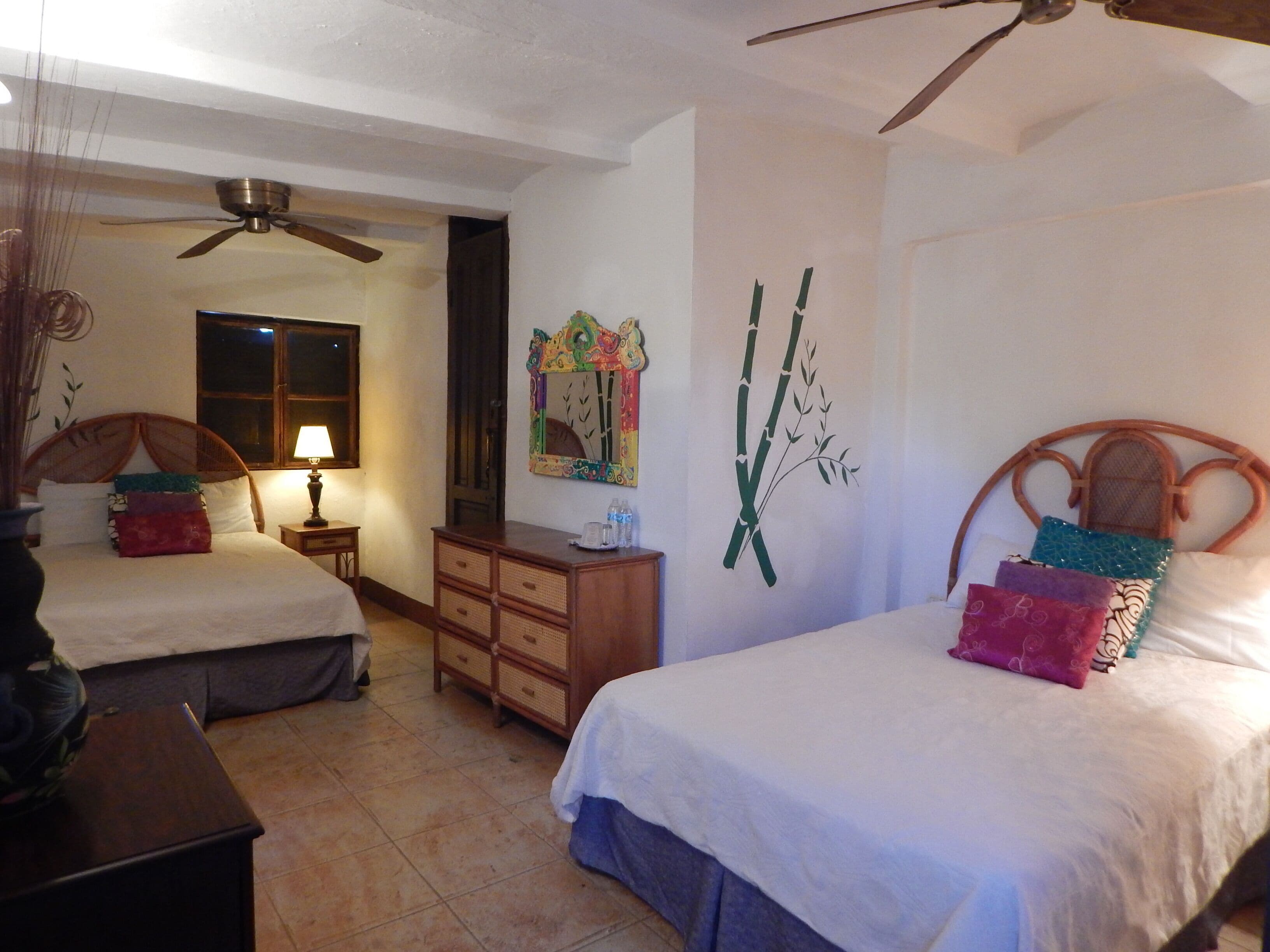 A hotel room with two beds, a ceiling fan, a dresser, and a wall with a bamboo decoration.