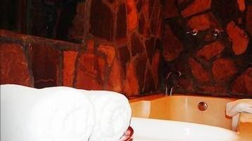 Un baño con pared de piedra, un lavabo rojo y toallas blancas, además de una bañera.