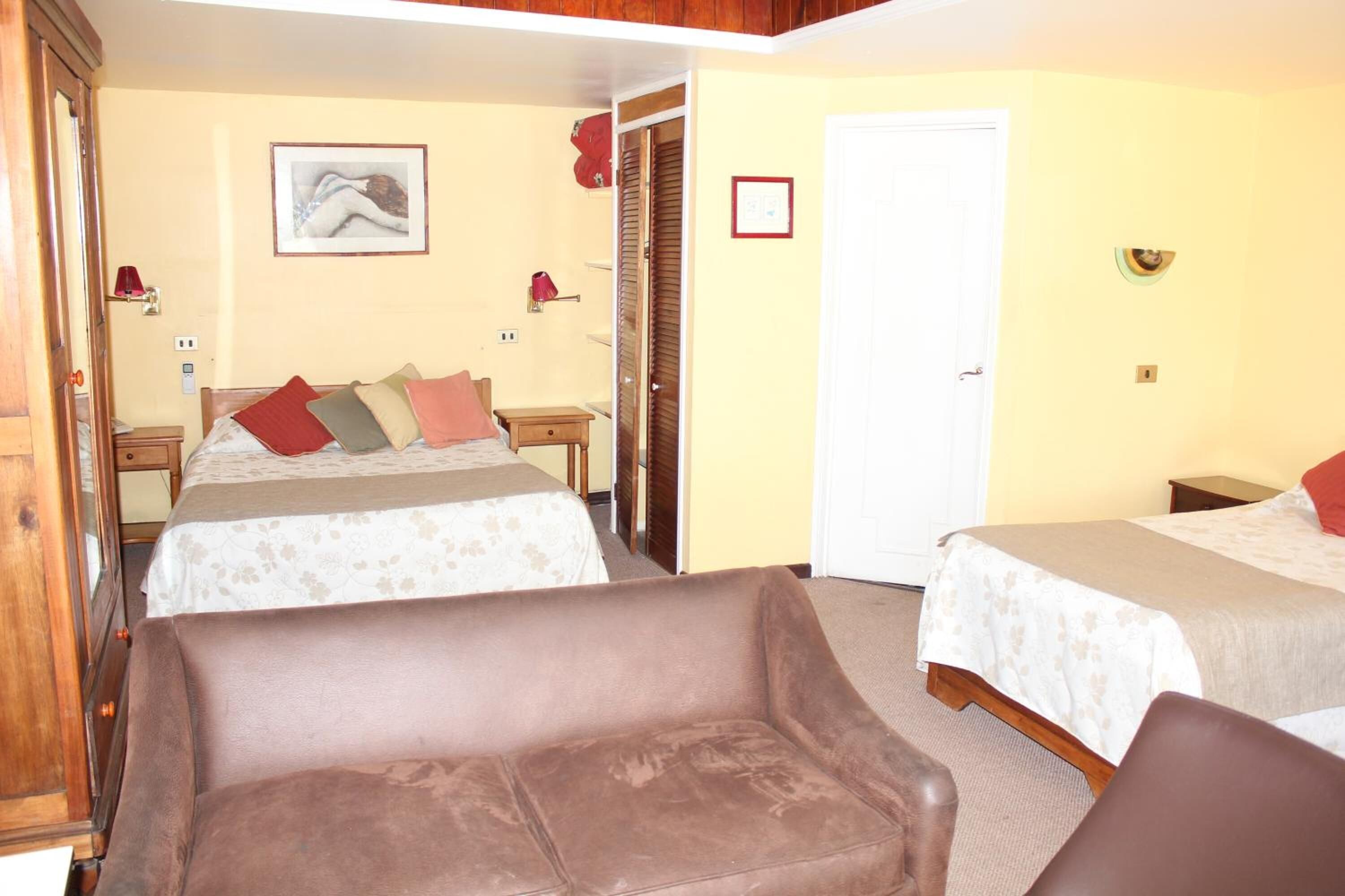 A room with two beds, a sofa, a wooden wardrobe, and a door.