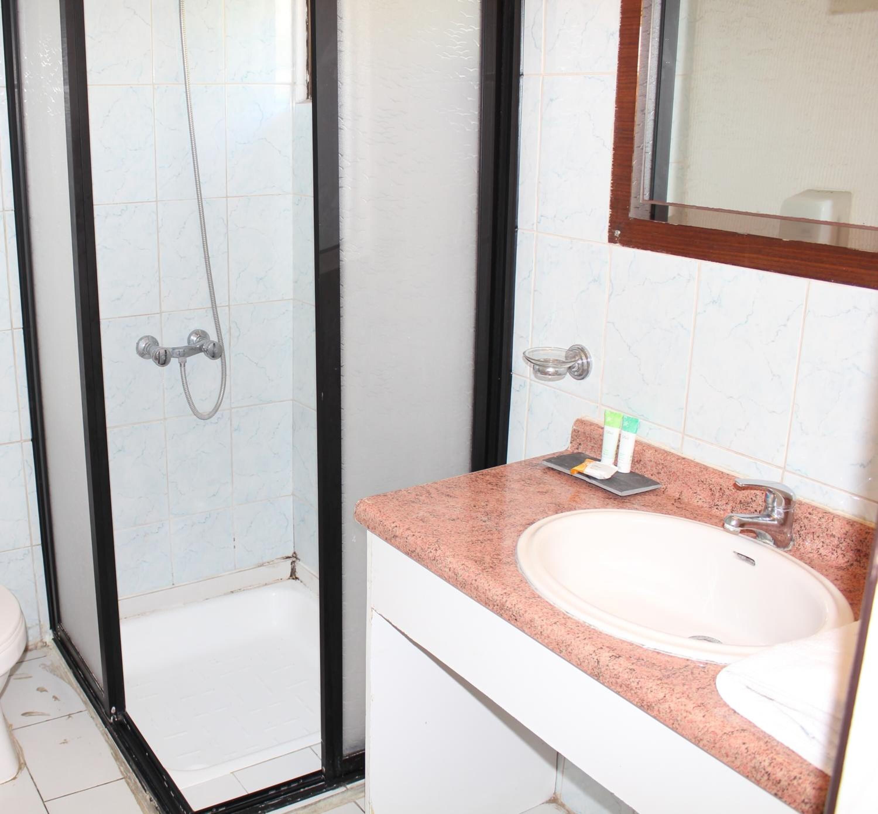 Un baño con ducha envuelta en vidrio, un lavamanos con encimera rosa y un espejo sobre el lavamanos.