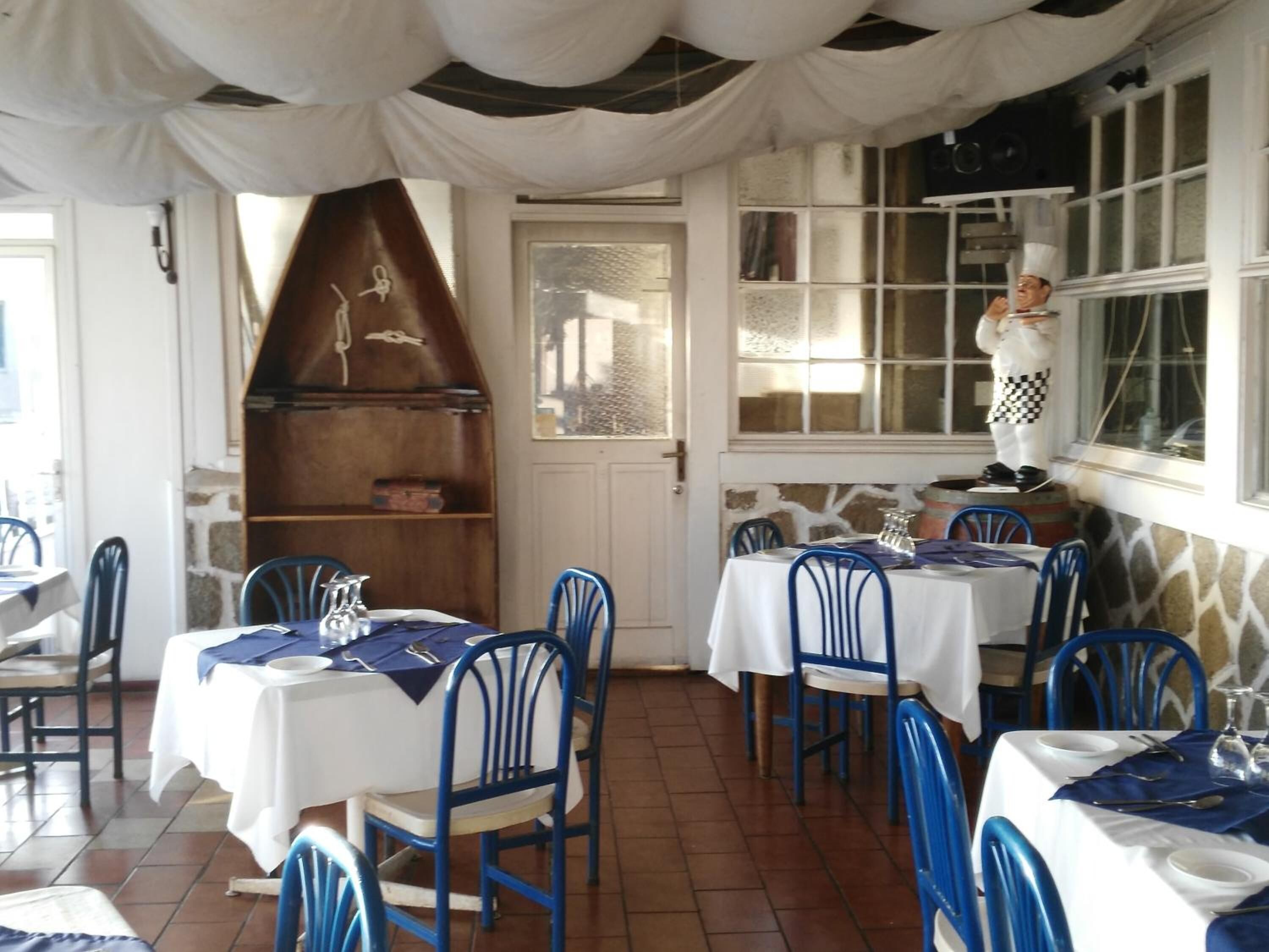 Een restaurantinterieur met tafels en stoelen, een kok bij het raam, en een stenen muur.