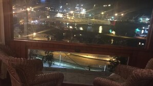 Vista desde una ventana con sillas de mimbre, con vista a un paisaje urbano nocturno donde se ven calles y edificios.