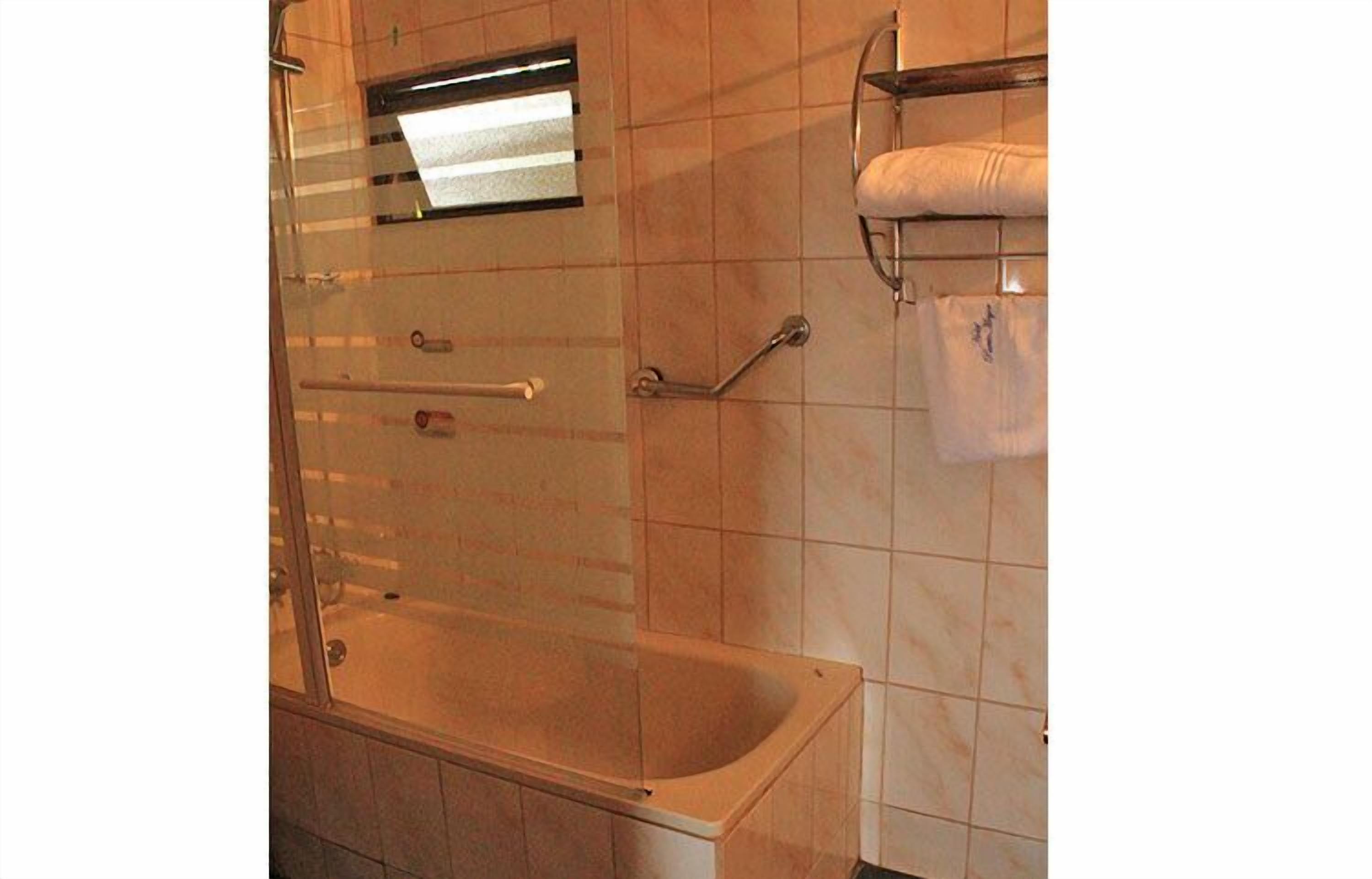 Un baño con bañera, cabina de ducha de vidrio, toallero y barandilla.