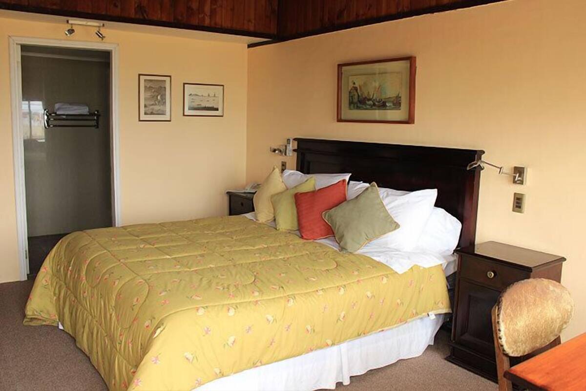 A bedroom with a bed, a nightstand, a lamp, a chair, and a door.