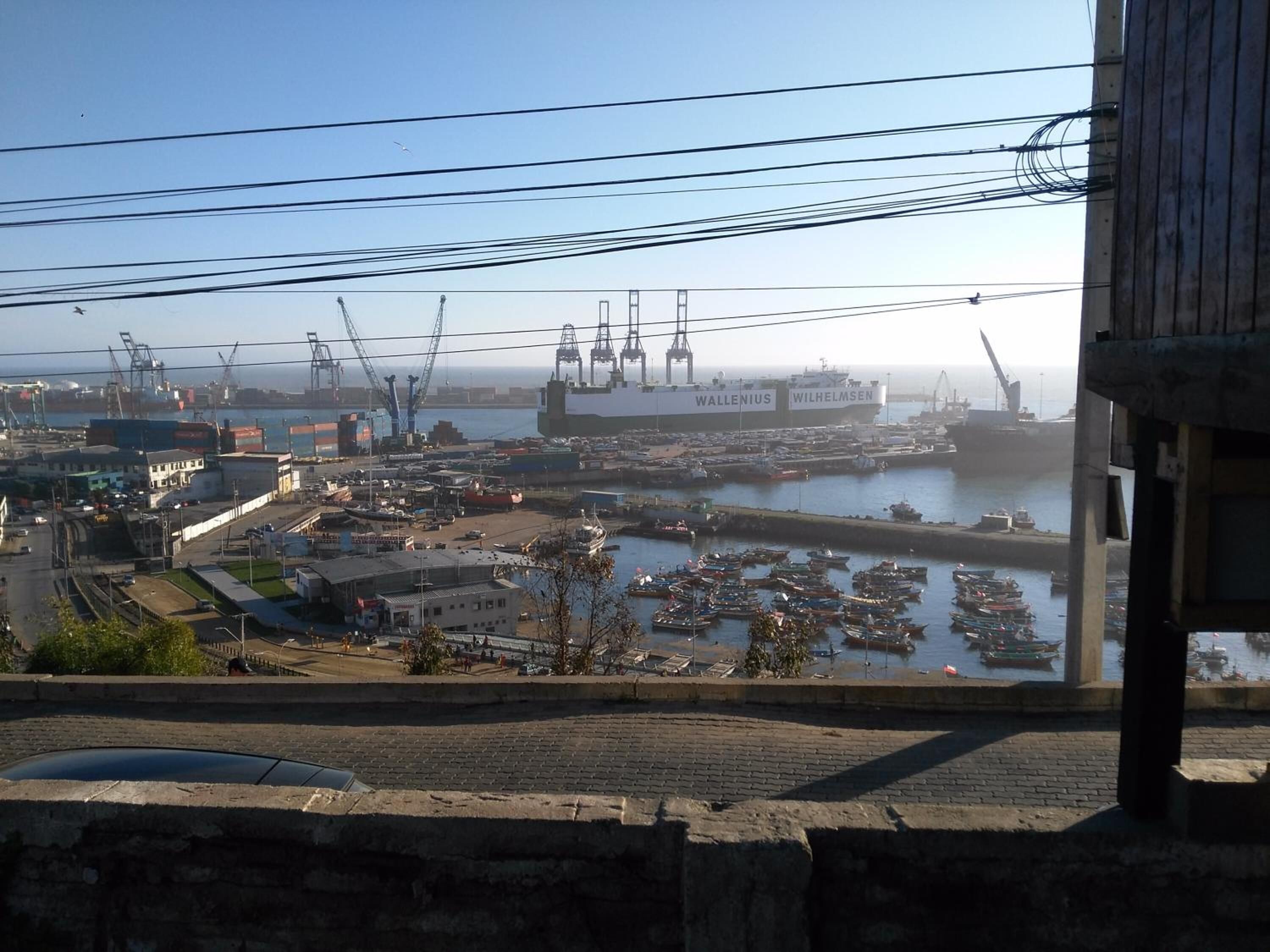 A harbor with multiple boats, a large ship named 'WALLENIUS' and 'WILHELM SEN', and industrial buildings.