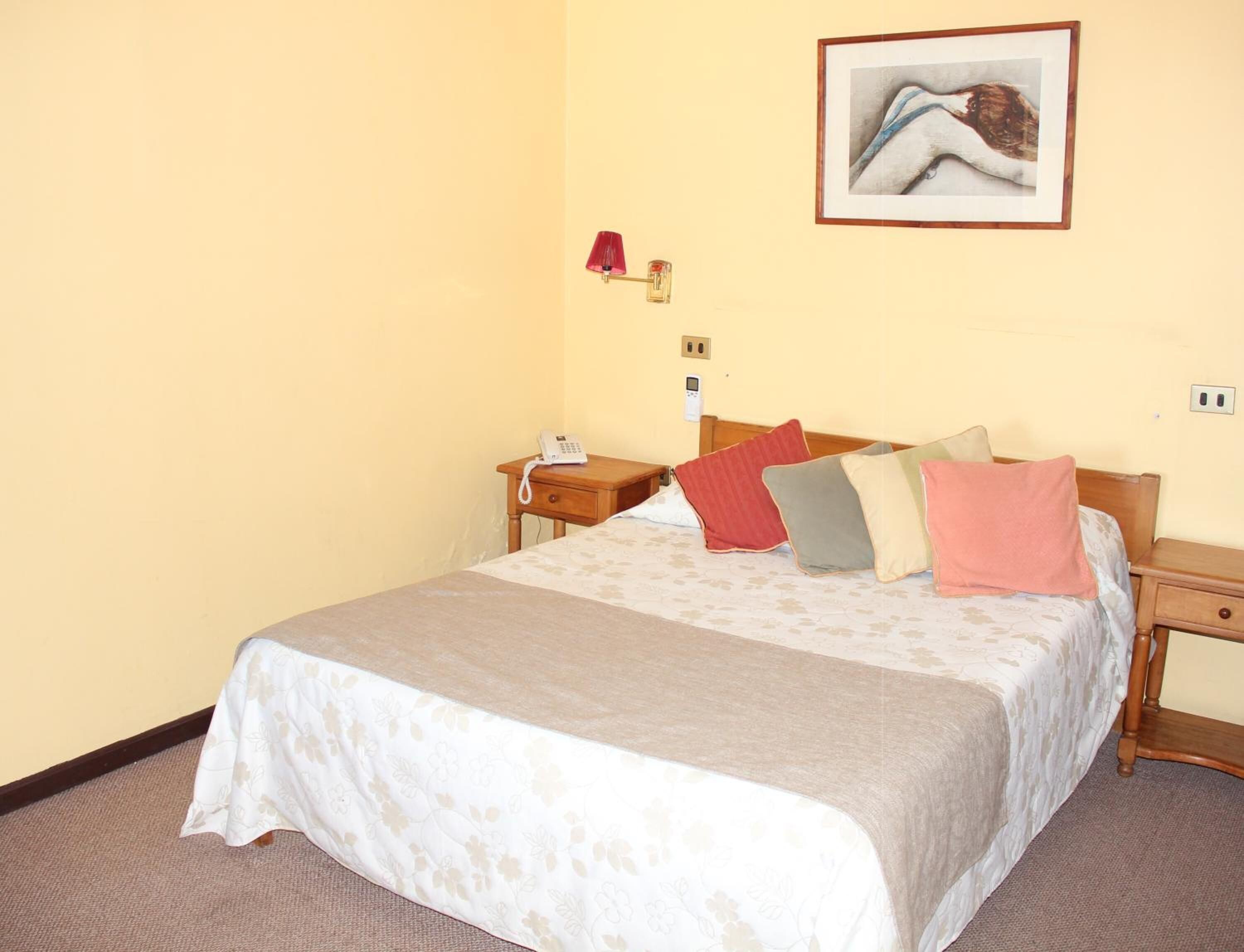 Una habitación de hotel con una cama, mesitas de noche, un teléfono y un cuadro en la pared.