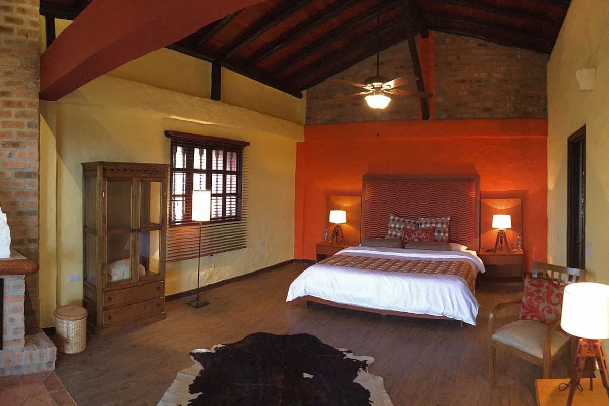 A spacious bedroom with a large bed, a fireplace, a wooden cabinet, and a rustic ceiling.