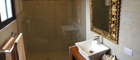 A bathroom with a glass-enclosed shower, a white sink with a gold-framed mirror, and a wooden vanity.
