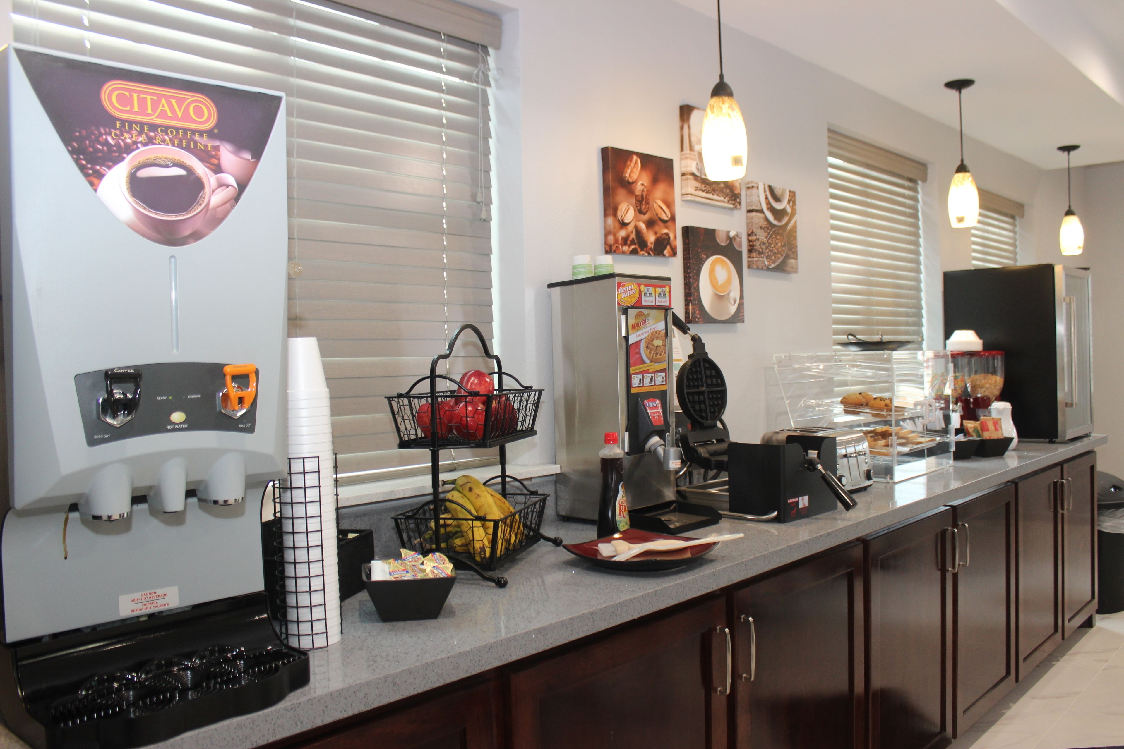 Een kitchenette met een koffieapparaat, een fruitmand en een ontbijtbalk.