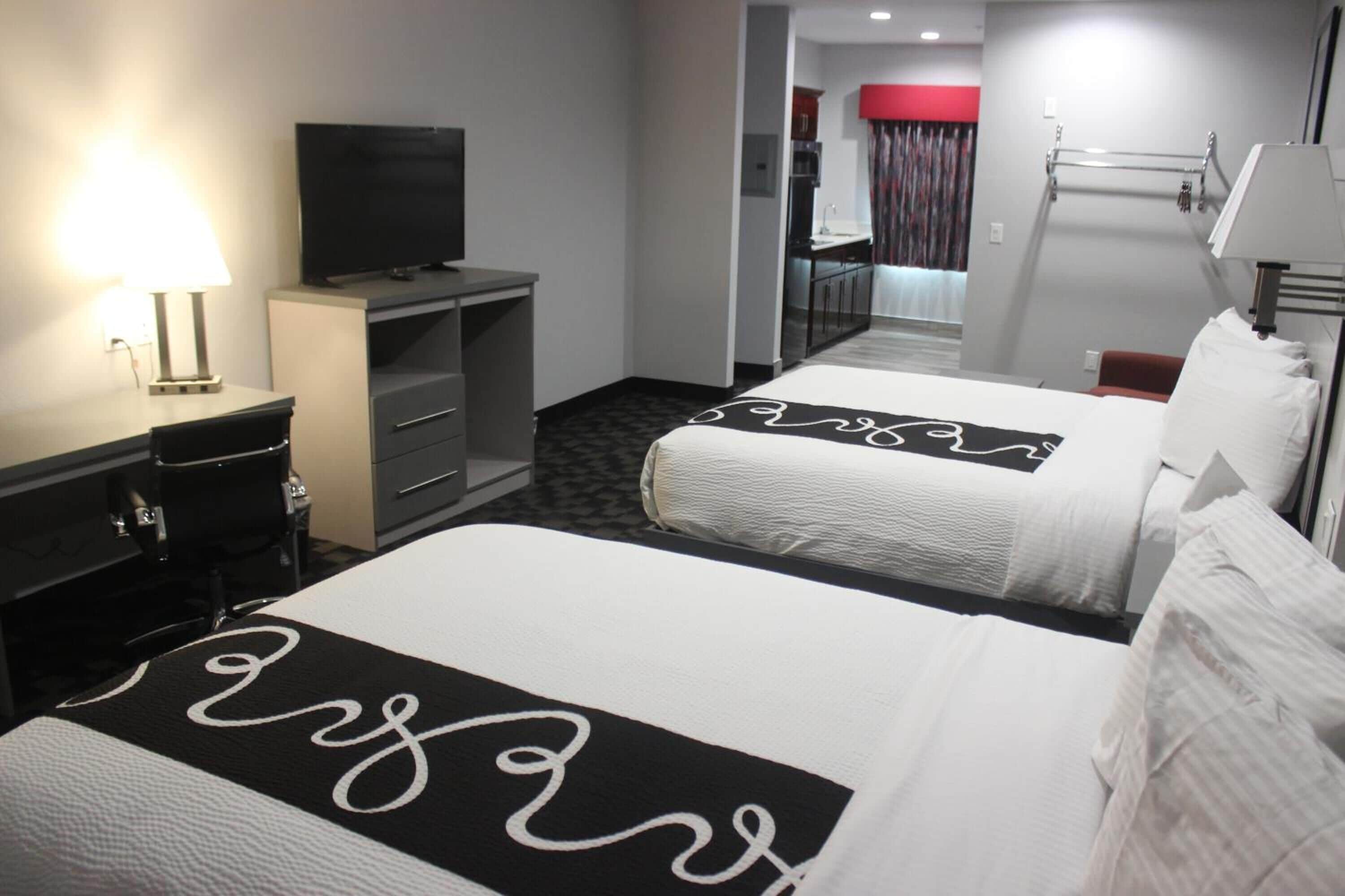 A hotel room with two beds, a desk with a television, a desk lamp, and a bathroom visible in the background.