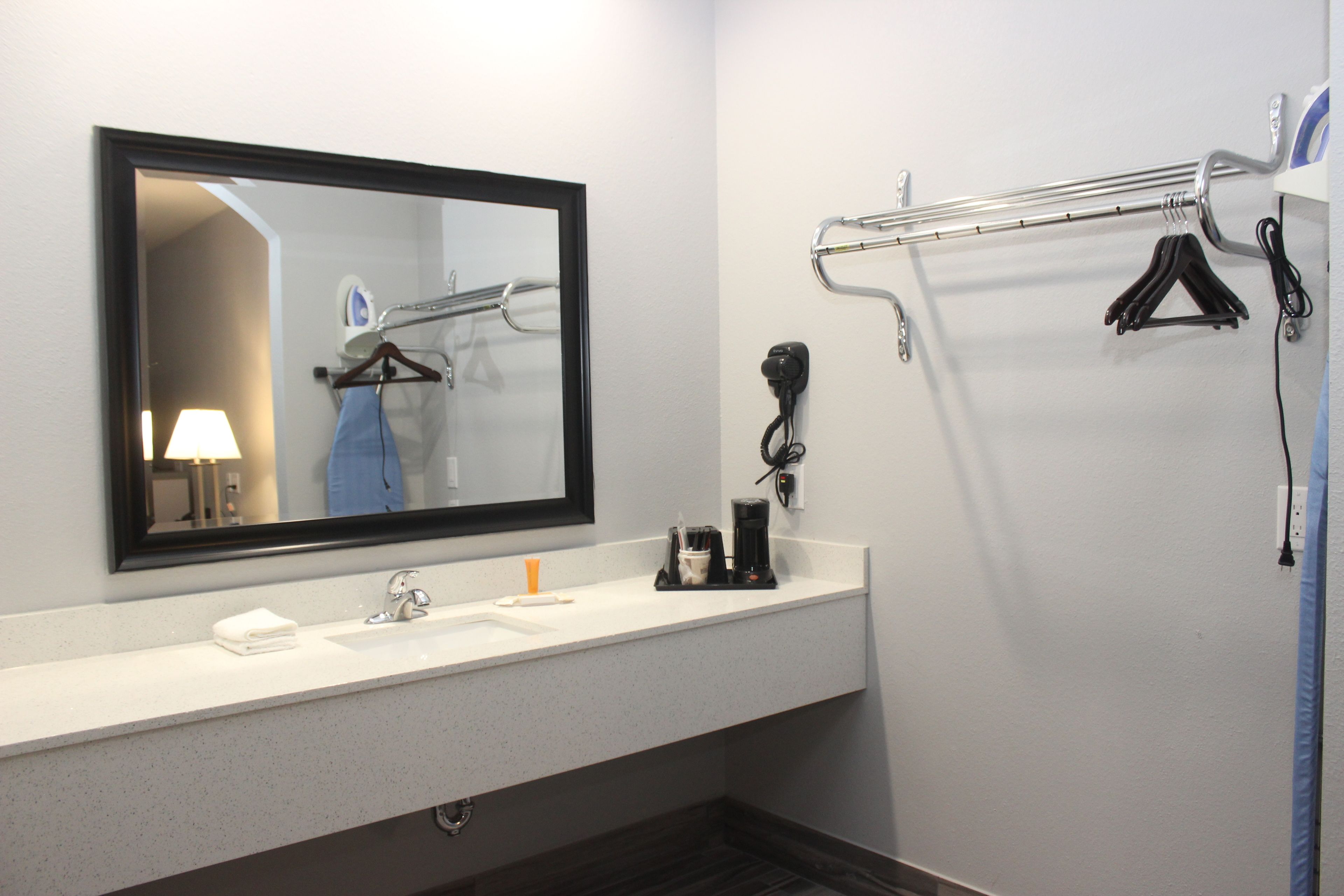 A hotel bathroom with a large mirror, a sink, a towel rack, and a hairdryer.