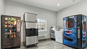 A kitchenette with a vending machine, a refrigerator, a washing machine, and a large Pepsi vending machine.