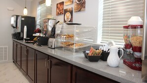 A breakfast bar with a coffee maker, toaster, and muffin display.