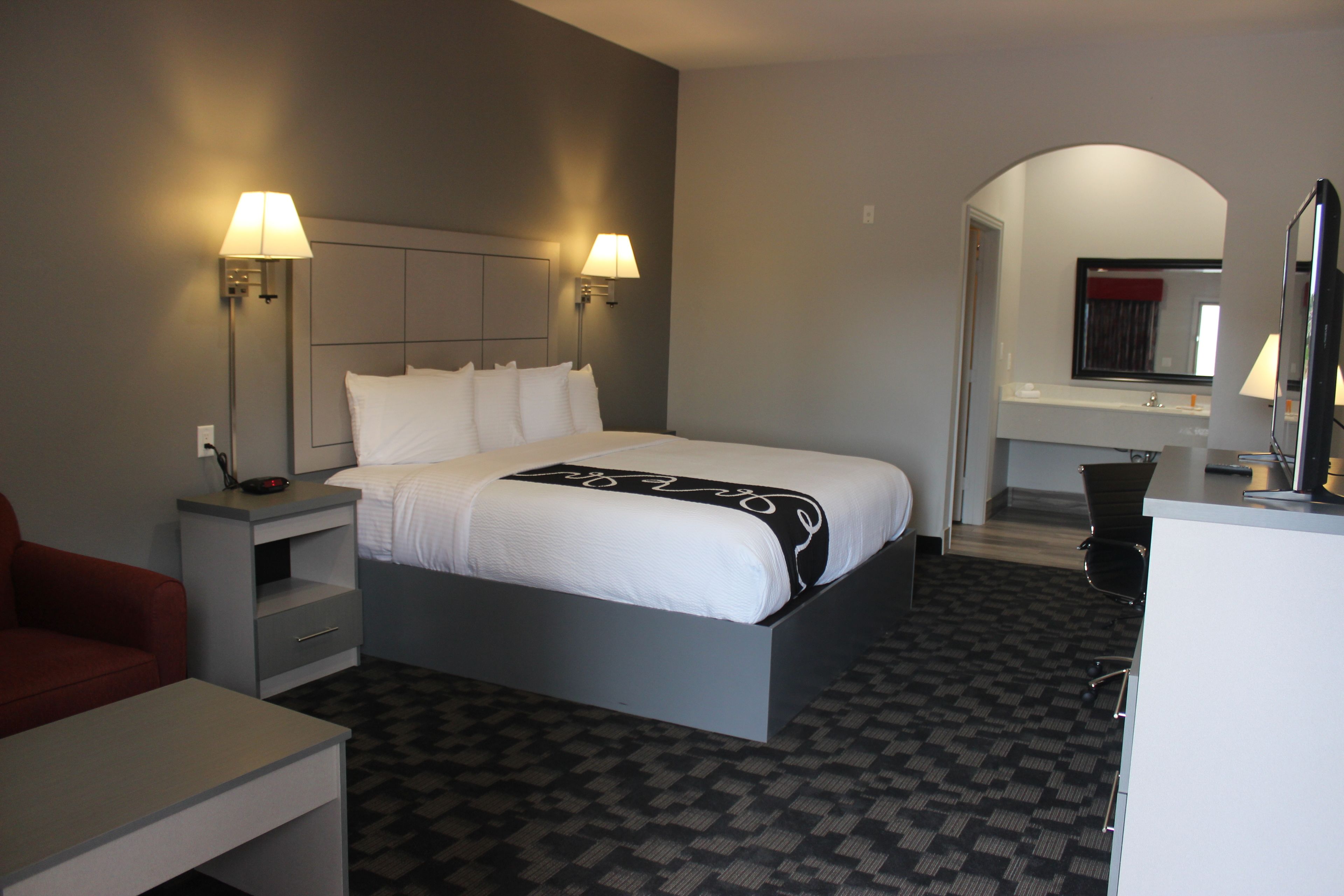 A hotel room with a large bed, two bedside lamps, a desk, and a chair.