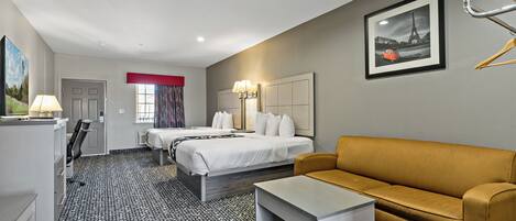 A hotel room with a bed, a sofa, a desk, and a lamp.