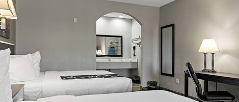 A hotel room with two beds, a desk, a chair, a mirror, and a lamp.